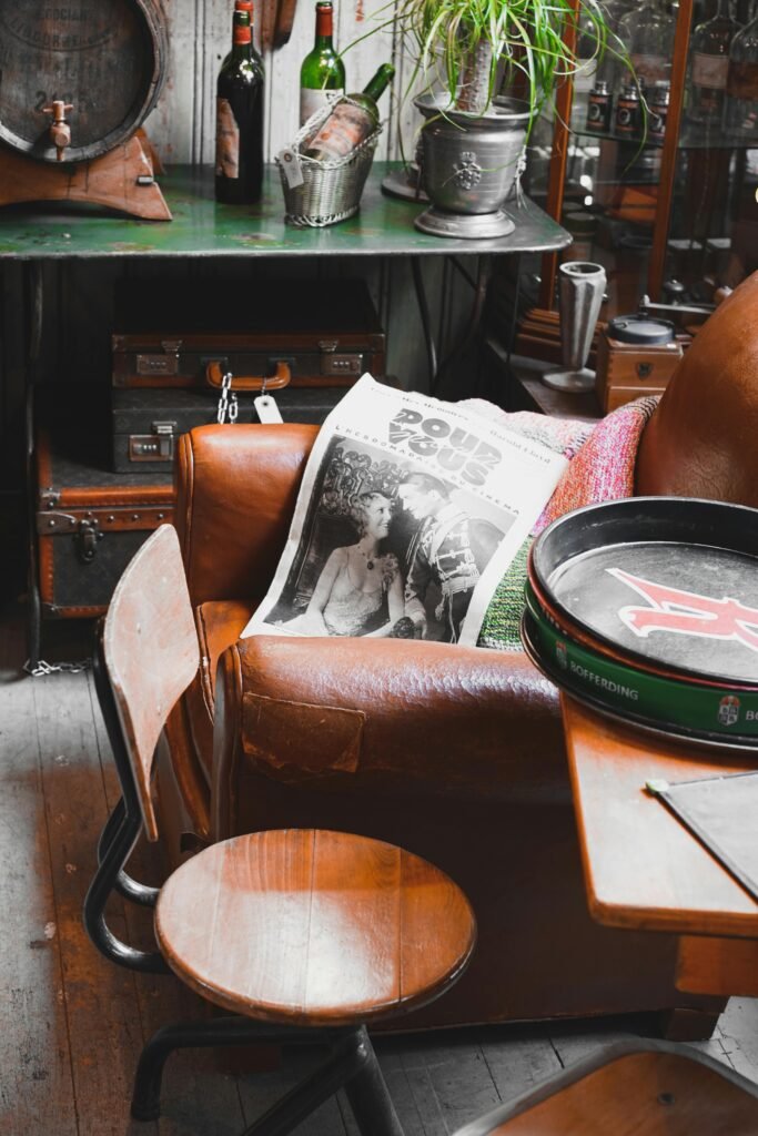A vintage-style room with a brown leather couch, wine bottles, a newspaper, and wooden furniture.